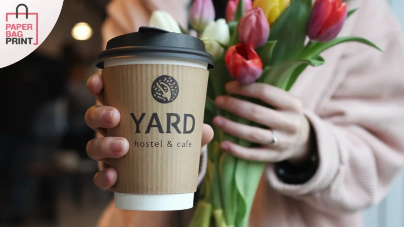 แก้วกาแฟกระดาษ YARD พร้อมดอกไม้หลากสีในมือ สื่อถึงความสดใสและอบอุ่น